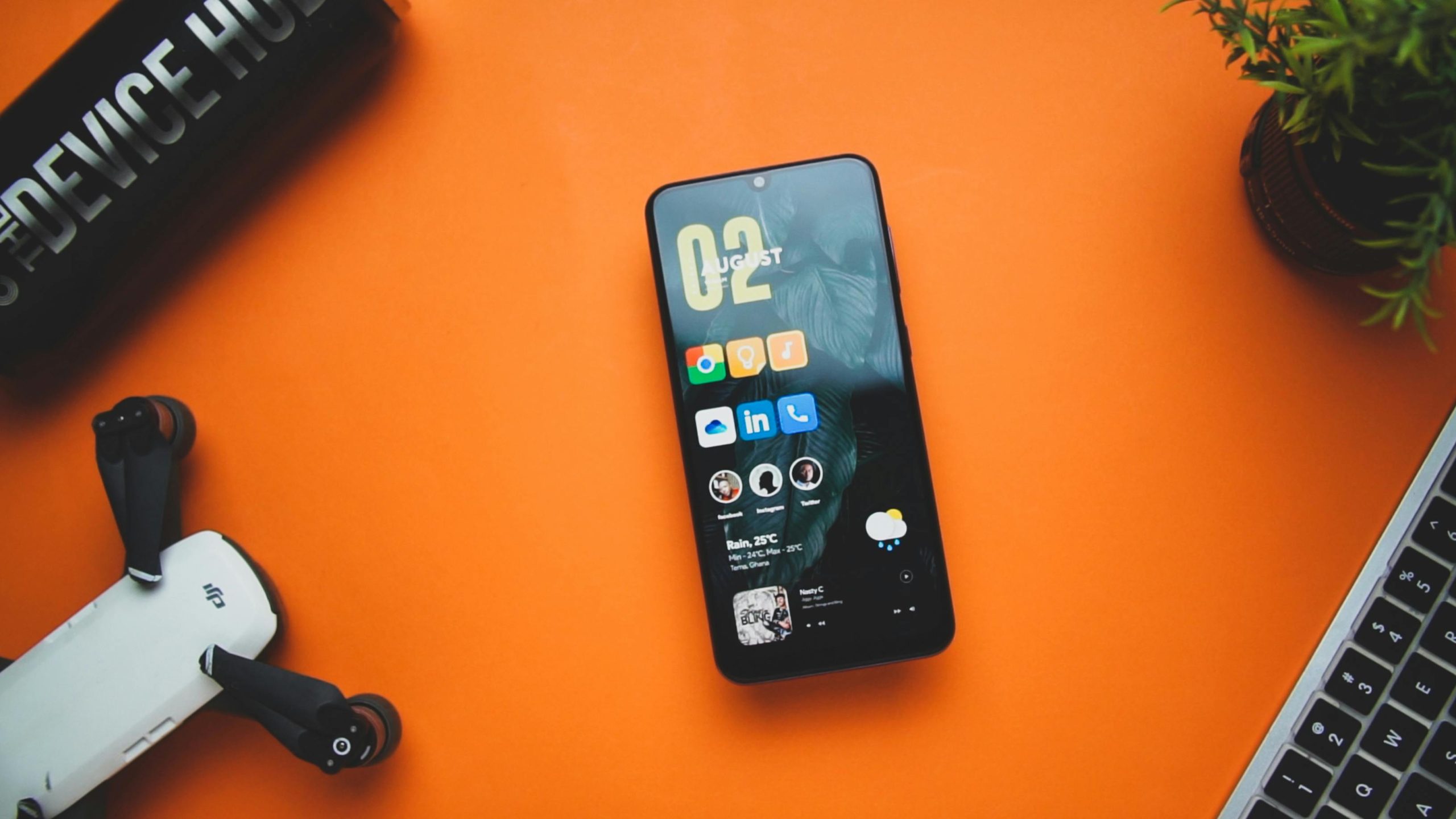 Flat lay of a smartphone with apps and a drone on an orange desk.